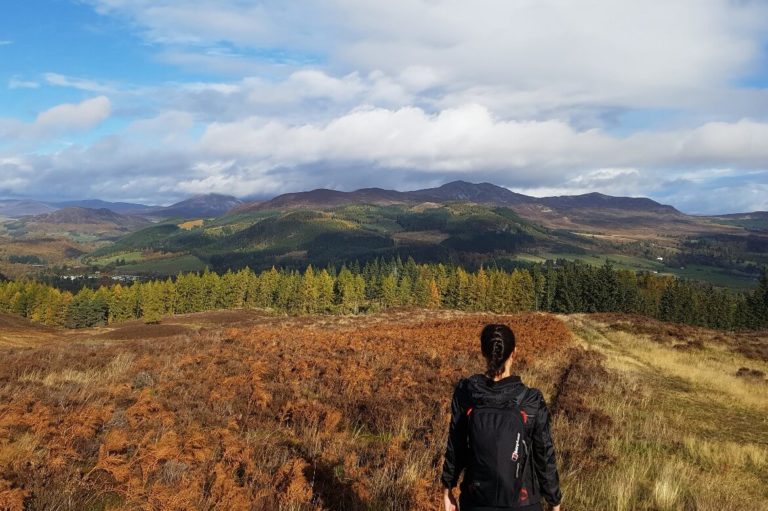 a woman walking towards the hills and forest